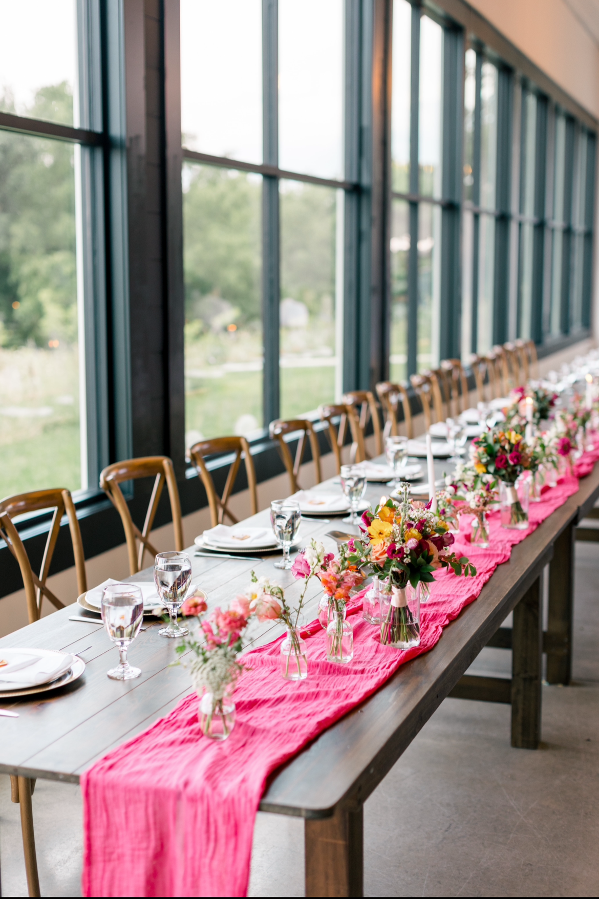 Head table for a wedding decorated with bud vases. Flowers are shades of pinks, yellows, and oranges.