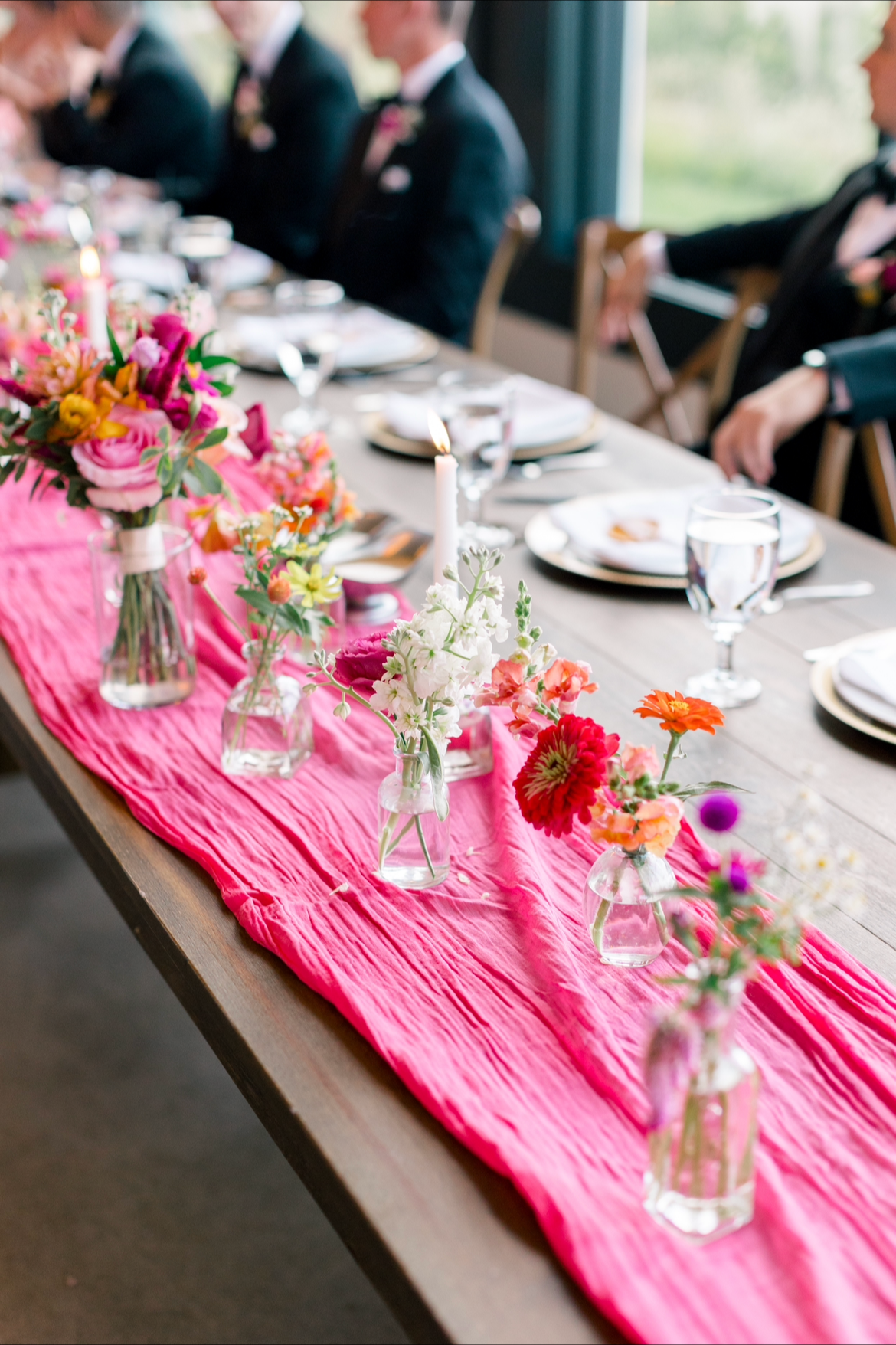 Example of a head table floral design for a wedding using bud vases. A variety of single stem flowers in bud vases in yellows, whites, reds, and pinks.