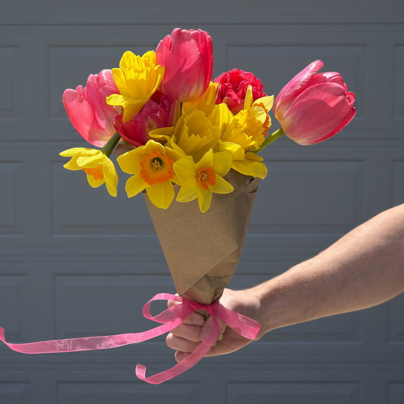 Person holding a bouquet of pink and yellow flowers with a pink ribbon in front of a door. Flowers grown locally in Ankeny Iowa at Rosie Days Flower Farm