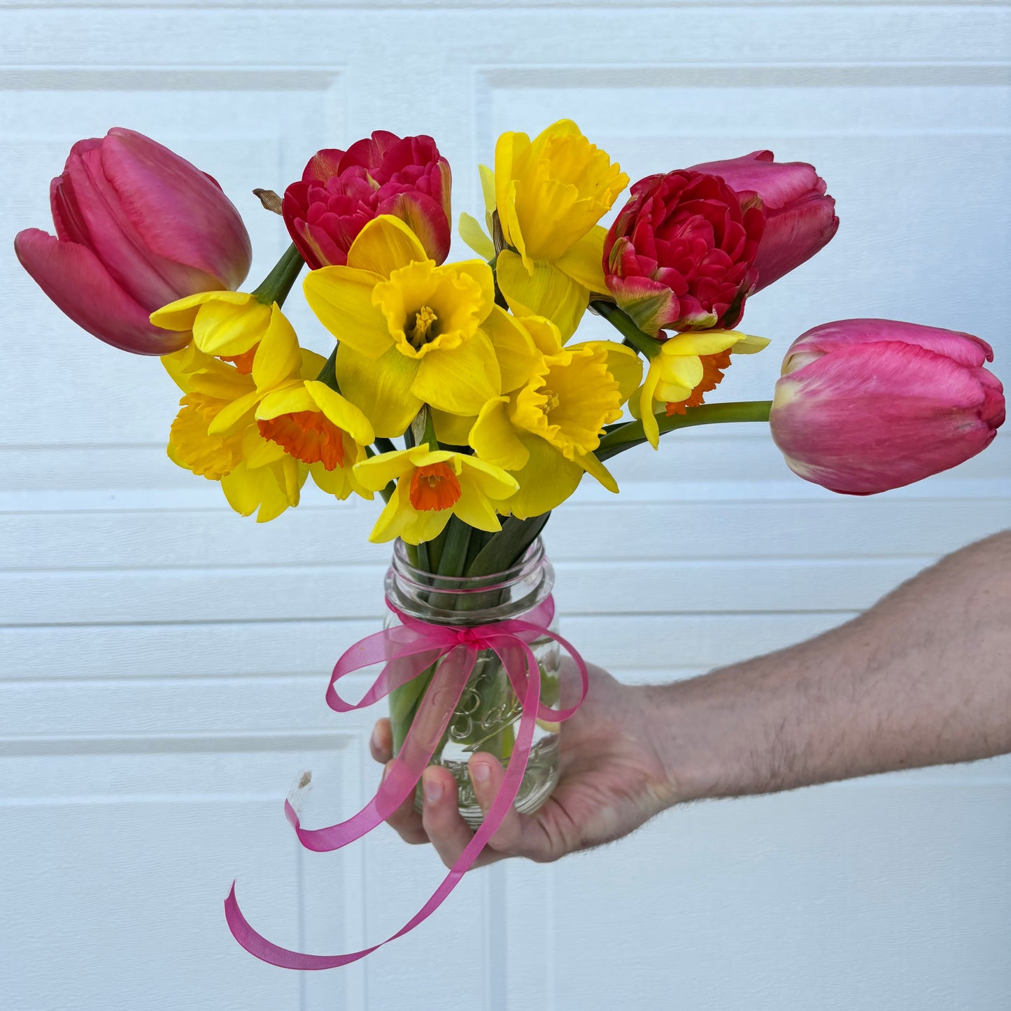 Bouquet of pink and yellow flowers held by a hand against a white paneled door.
